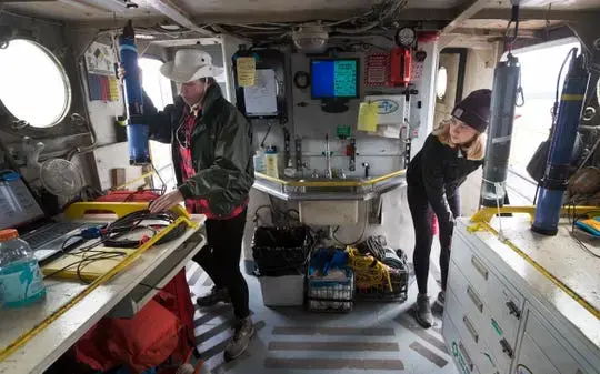 Graduate student Emma Ray, left, and undergraduate research assistant Tosh Sook measure water quality of Green Bay aboard the Neeskay, a UW-Milwaukee research vessel. The student researchers were measuring dissolved oxygen in the bay for a long-term water monitoring project. Image by Mark Hoffman. United States, 2019.
