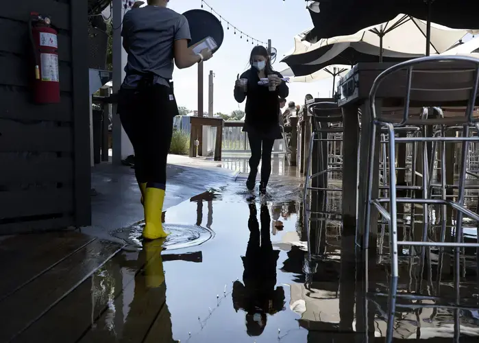 Servers Alexandra Schroettner and Christi Hughes wade through salt water that has risen over the patio at Saltwater Cowboys as they serve guests lunch on Shem Creek on Monday, Sept. 21, 2020, in Mount Pleasant. Image by Grace Beahm Alford / Post and Courier. United States, 2020.