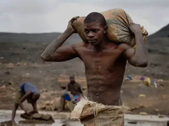 A miner carries a bag of slag toward a waiting truck. The slag will be sold for reprocessing. Image by Larry C. Price. Zambia, 2017.