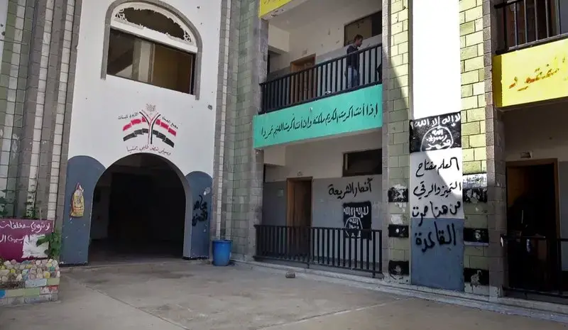 The black al-Qaida flag and the slogan in Arabic “al-Qaida passed here,” on the right wall, are sprayed on a damaged school that was turned into a religious court in the southern city of Taiz. Image by AP. Yemen, 2017.