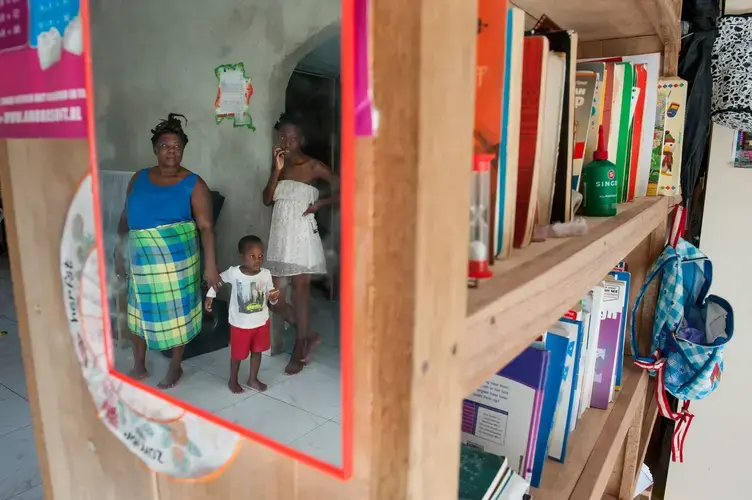 The family of Frans Weewee is reflected in a mirror at the home they are building in a village in Brownsweg. Weewee moved his family from the Netherlands back to Suriname and is aiming to start a radio station, in part to rebuild the traditional Saamaka culture that was displaced by the flooding of the Brokopondo Reservoir and now is lured by the promise of a gold rush. Image by Stephanie Strasburg. Suriname, 2017.