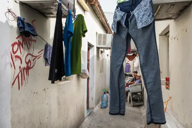 LEFT HANGING. The workers stay in a camp without being paid since January 2017. They cannot afford to pay for a taxi to go downtown. Most of the days they stay inside the camp. Here, two workers sit outside, amid drying laundry. Image by Hans Lucas. Qatar, 2017.