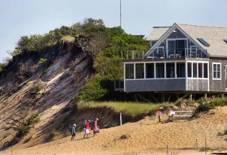 A home sat close to the edge of an eroding dune on Ballston Beach in Truro. Image by John Tlumacki. United States, 2019.