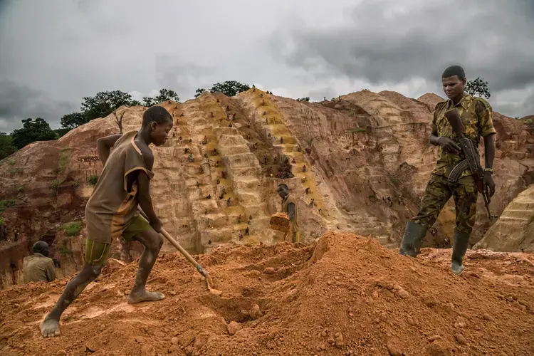 A Muslim rebel stands guard as men and boys dig for gold at a mine near Bambari. The rebels claim a share for “security.” Gold is plentiful in the Central African Republic, but corruption and political instability have kept the profits from benefiting the people. Image by Marcus Bleasdale. Central African Republic.