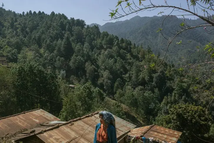 In Paraje León, a village of three hundred people, in a remote corner of Totonicapán, a woman stands outside her house, situated in front of a reforested mountain. Image by Mauricio Lima. Guatemala, 2019.