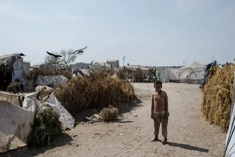 A Yemeni boy walks through the sand back to his tent in Mishqafa Camp on April 23, 2018. Most of the families in the camp come from impoverished areas near the front line, but the camp is also destitute. Image by Alex Potter. Yemen, 2018.