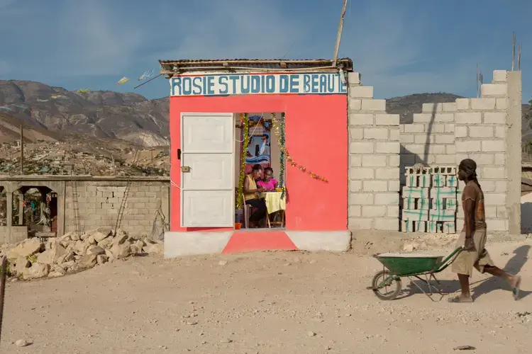 Rosemanie 'Rosie' Prospere, 35, left, manicures the nails of her assistant Dieuny Delizin, 19, at her beauty salon in the Canaan 5 neighborhood. Prospere came to the area in 2015 with a dream of opening a salon of her own. Now almost four years later, she says that business is hard but at least she is not stressed about having to make rent. Now she dreams of opening a chain of beauty salons all across the region – all pink, of course. 'When you have a business, you have to make it stand out,' Prospere says. Image by Allison Shelley. Haiti, 2019.