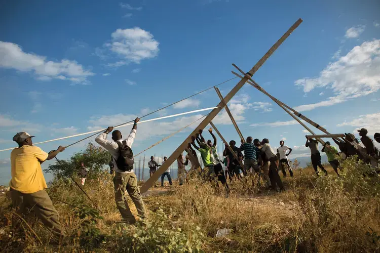 Residents of Canaan raise the first of three handmade utility poles, part of an improvised effort to receive electricity from the state power grid. Image by Allison Shelley. Haiti, 2017.<br />
