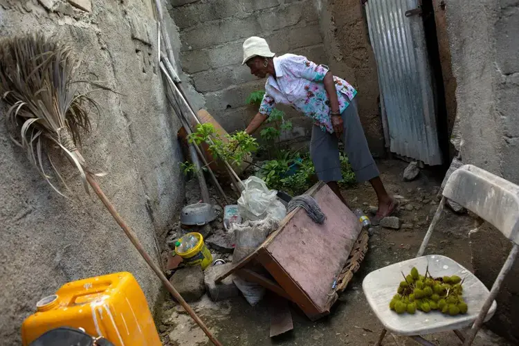 Farmer Rose Marie Fidele, 73, tends to the few plants she can coax to grow in a little urban space behind the home she shares with her son and his family near Caracol, Haiti, December 10, 2019. Image by Allison Shelley. Haiti, 2019.