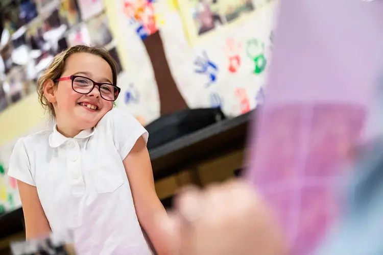 Ava Brenna, 7, of Possilpark, smiles as she looks up at a paper being held by Kelsey Reilly as they make vision boards during an arts and crafts session at Possilpoint Community Centre. Image by Michael Santiago. United Kingdom, 2019.