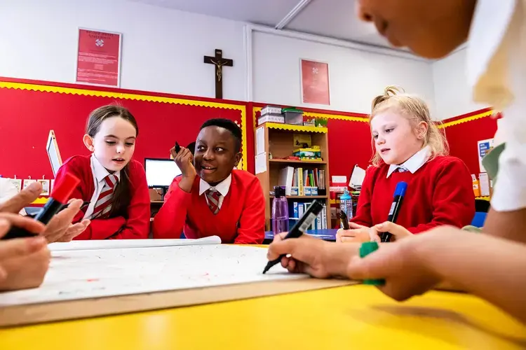 From left to right: Holly Muir, 9, Hanford Frimpong, 11, and Summer McKay, 10 — all of the Bridgeton neighborhood of Glasgow, Scotland — listen as Stacy Innerst, children’s book illustrator, speaks about his work, at Sacred Heart Primary School in Glasgow. Image by Michael Santiago. United Kingdom, 2019.