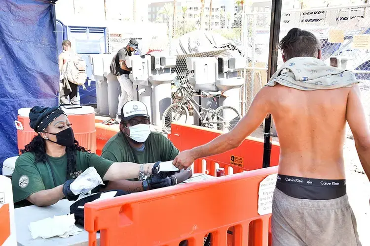 A homeless man receives a face mask on June 24 at the Lots in Phoenix. Hand-washing stations, restrooms and access to cold water are advertised benefits of the encampment, and social distancing is encouraged. Image by Steve Carr/Human Services Campus. United States, 2020.<br />
