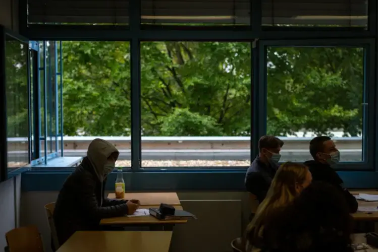 Students sit in classroom at a secondary school in Brühl, Germany, outside of Cologne, with windows wide open to provide air circulation. Ventilation is an official part of the government’s strategy to prevent Coronavirus spread in schools. Older students are again required to keep masks on all day as cases in the state of North Rhine-Westphalia rise. Image by Ryan Delaney/St. Louis Public Radio. Germany, 2020.