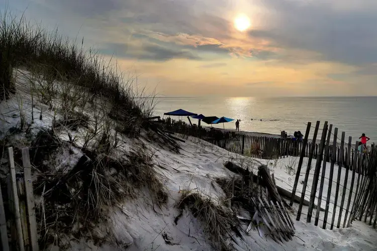 The sun began to set over Mayflower Beach at high tide. The fencing put up along the dunes helps to catch the blowing sand and mitigate erosion. Image by John Tlumacki. United States, 2019.