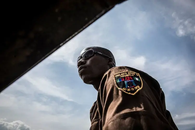 A member of the Vigilante Group of Nigeria rides on the back of a patrol truck during a meditation meeting, going to the area where a herd of cattle destroyed a maize field in Barkin Ladi on Oct. 24. Image by Jane Hahn. Nigeria, 2018.