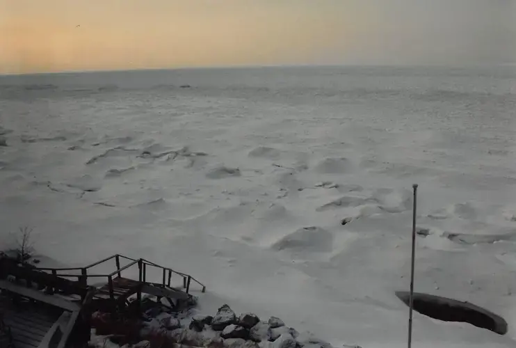 This is a photo of the ice shelf extending out from the beach at Nancy Schwab's vacation home in the early 1990s. As the Earth warms, that ice shelf is not there to protect the beaches and dunes along Lake Michigan from erosion. Courtesy of Nancy Schwab.