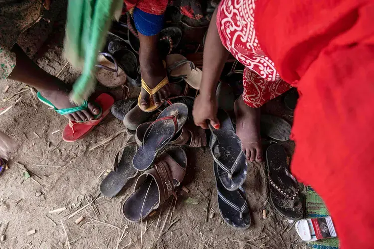In this July 26, 2019 photo, Ethiopian migrant girls put on their slippers to go and eat outside their lockup known in Arabic as a 'hosh,' in Ras al-Ara, Lahj, Yemen. Some lockups hold as many as 50 women at a time. The women will stay here for several days until their transportation is ready. Image by Nariman El-Mofty / AP Photo. Yemen, 2019.