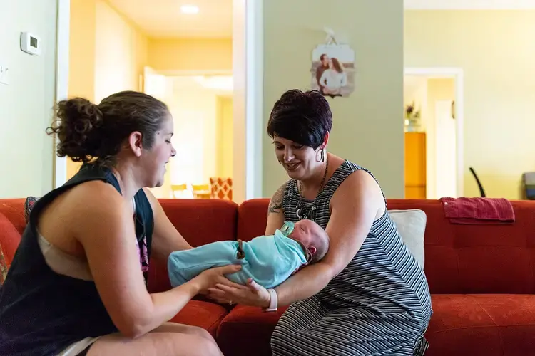 Hailey Frazier (left) gives her son Isaac to Sabrina Elliott (right), a doula in Abilene during a home visit. Image by Gary Rhodes for The Texas Tribune. United States, 2018.
