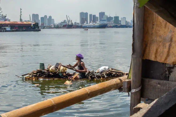A woman scavenges for wooden planks in Manila Bay to turn into lump charcoal she can sell. Image by Micah Castelo. Philippines, 2019.