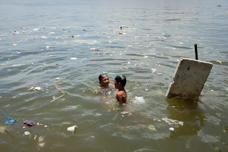 On a hot summer day, children swim in Manila Bay’s murky waters amid floating pieces of plastic and Styrofoam. Image by Micah Castelo. Philippines, 2019.