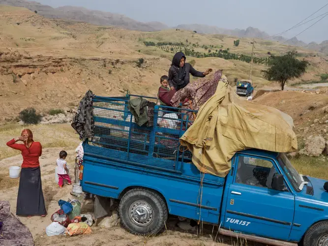 Unable to afford the cost of renting a large truck to make their move easier, some Zamani family members must walk while a pickup carries their belongings, the elderly, and kids. In recent years many families have stopped moving and living as nomads because of the hardships. For others, raising animals provides the only income. Image by Newsha Tavakolian. Iran, 2018.