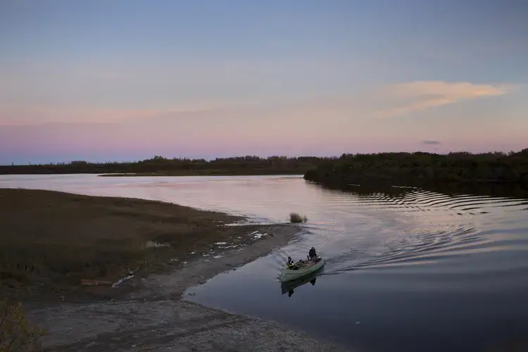 A family returns by canoe from cutting firewood in Attawapiskat, Ontario, in preparation for the cold, long winter ahead. Attawapiskat is an isolated First Nation community located in northern Ontario, Canada, at the mouth of the Attawapiskat River on James Bay. In 2016, the community of approximately 2,000 people declared a state of emergency after being overwhelmed with attempted suicides, over 100 attempts in a 10-month period. Image by David Maurice Smith/Oculi. Canada, 2016.