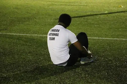 A player ties his shoe at team practice for the Chagos Islands National Team. Image by Kristen Popham. United Kingdom, 2019.