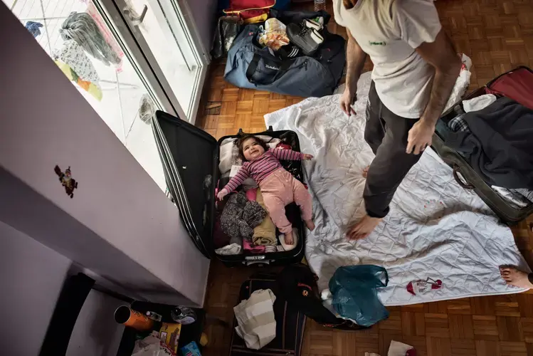 Syrian refugee Muhanned Abzali, jokes with his 6 month old daughter, Heln, by packing her in a suitcase, the night before leaving for relocation in Estonia. Image by Lynsey Addario. Greece, 2017.