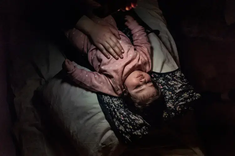 Syrian refugee Heln is rocked to sleep with the light of an iphone by a Syrian refugee friend of Taimaa, the night before the family travels from Athens to Estonia for relocation. Image by Lynsey Addario. Greece, 2017.