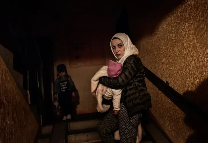 Syrian refugee Taimaa Abzali weeps as she holds baby Heln and enters her new apartment building after a long, grueling day of travel and upheaval once again from Athens to their new home in Polva, Estonia. Image by Lynsey Addario. Estonia, 2017.