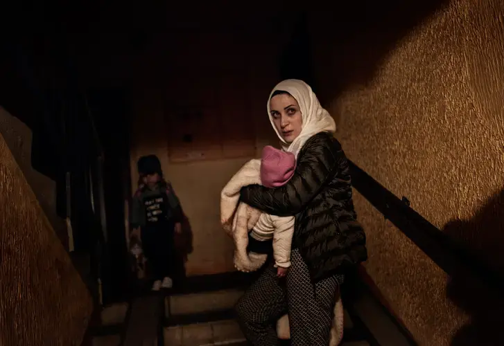 Syrian refugee Taimaa Abzali weeps as she holds baby Heln and enters her new apartment building after a long, grueling day of travel and upheaval once again from Athens to their new home in Polva, Estonia. Image by Lynsey Addario. Estonia, 2017. 