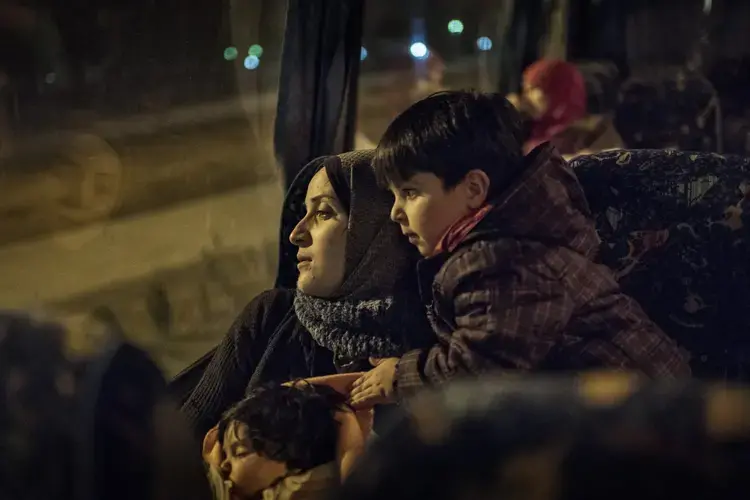 Syrian refugee Taima Abazli, 24, sits with her two children: baby Heln, 4 months old, and Wael, 3 years old, as they ride on the bus with other refugee families to Athens to attend an appointment regarding their asylum case the following morning. Image by Lynsey Addario. Greece, 2017.