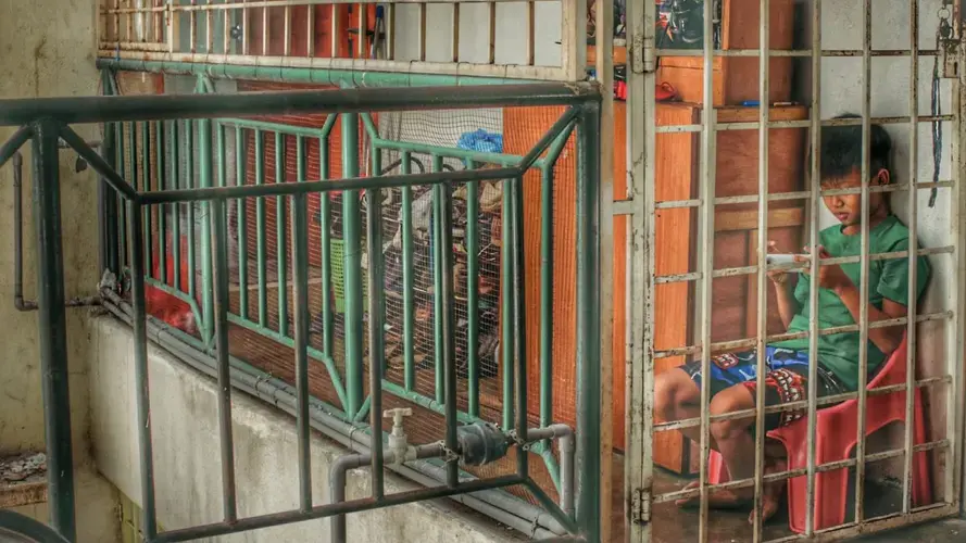 A Chin refugee from Myanmar sits on his balcony in Kuala Lumpur. He stayed home for weeks without going outside or attending school. Image by Benjamin. Malaysia, undated.