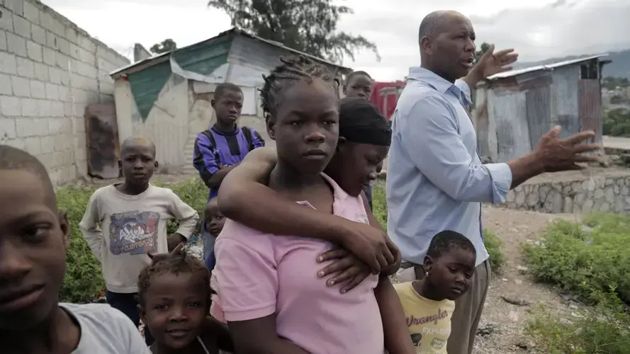 Cami Etienne, far right, talks about the situation in Haiti in the company of some of the children who live in a makeshift camp located off a dirt road in the interior of Delmas. Image by Jose A. Iglesias. Haiti, 2019.