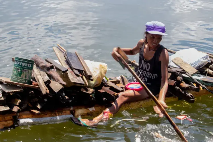 A woman scavenges for wooden planks in Manila Bay to turn into lump charcoal she can sell. Image by Micah Castelo. Philippines, 2019.