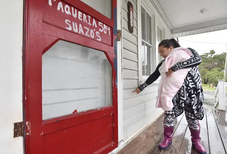 Jade Lopez carries her daughter Soany and shows where the floodwaters of Hurricane Dorian reached at her business on Creek Road. Image by Dylan Ray. United States, 2020.