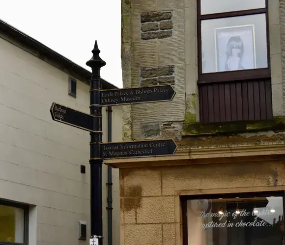 Orkney is a popular tourist destination with several historic attractions. In Kirkwall's Town Center, a sign in front of a barber shop points to the Earl's Palace and Bishop's Palace—ruins near the island's coast—and the St. Magnus Cathedral, founded in 1137. Image by Maggie More. United Kingdom, 2020.