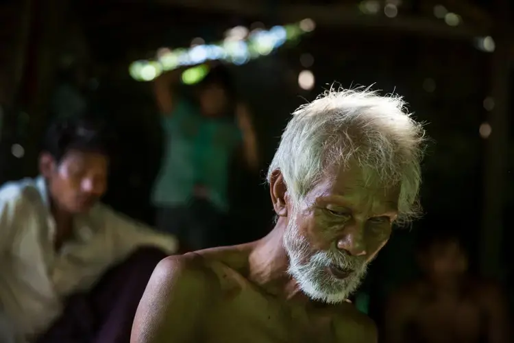 U Hla Myint, 65, sits in his home in a small village where migrant workers for Supowin Palm Oil live outside Kawthaung, Myanmar. U Hla Myint and his wife retired five years ago. They're now supported by two sons. Image by Taylor Weidman/PRI. Myanmar, 2016.