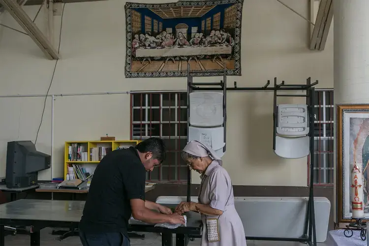 A nun helps a patient with his medication at the Our Lady of Guadalupe Migrant Home in Reynosa, Mexico, on May 2, 2017. According to the director of the shelter, the majority of the people staying at the shelter are recent deportees from the United States. Image by Meghan Dhaliwal. Mexico, 2017.