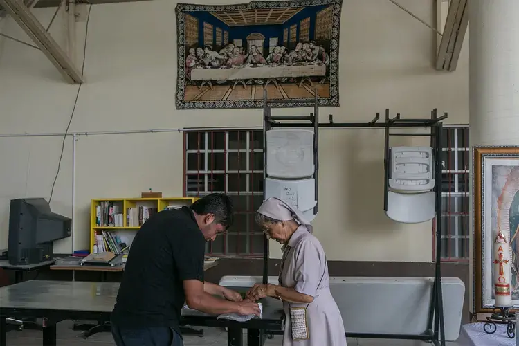 A nun helps a patient with his medication at the Our Lady of Guadalupe Migrant Home in Reynosa, Mexico, on May 2, 2017. According to the director of the shelter, the majority of the people staying at the shelter are recent deportees from the United States. Image by Meghan Dhaliwal. Mexico, 2017.