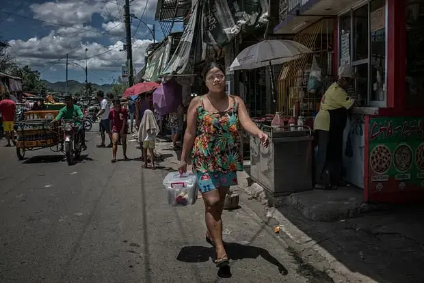 Rhoda, a widow who is raising seven children after her husband was killed in an extrajudicial killing, walks through the streets of Payatas to deliver an Avon product, which she started selling door to door in January 2018. Image by James Whitlow Delano. Philippines, 2018.