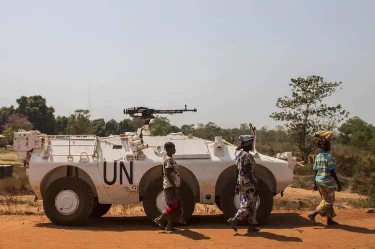 Women walk past a U.N. vehicle at the entrance to the sprawling camp in Kaga-Bandoro for thousands of families displaced by civil conflict. Image by Jack Losh. Central African Republic, 2018.