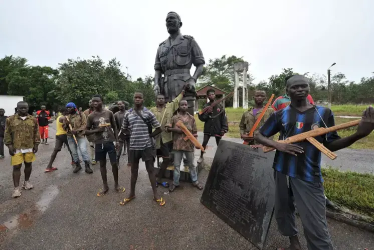 Ex-Seleka rebels with wooden weapons stand next to a statue of Emperor Bokassa at his Berengo palace in 2014. Image by Sia Kambou. Central African Republic, 2014.
