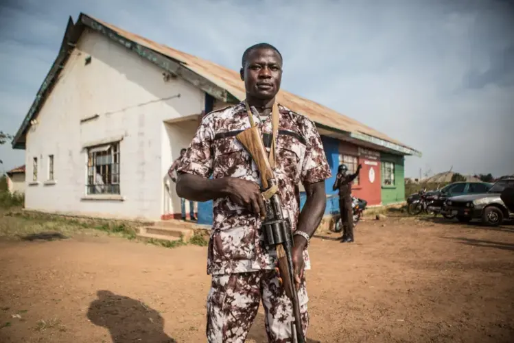 Bitrus Goting, 29, who joined the volunteer peacekeepers in Barkin Ladi in 2012, carries a homemade rifle outside the group’s headquarters. Image by Jane Hahn. Nigeria, 2018.