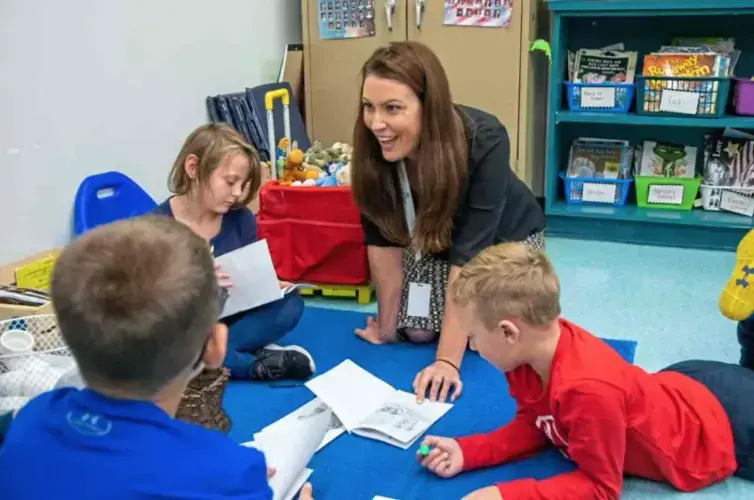 Sara Ruffner, a Literacy Outcomes Specialist for Learning Ovations, helps students with a reading activity in a first-grade classroom at David Leech Elementary. Image by Andrew Rush. United States, 2019.