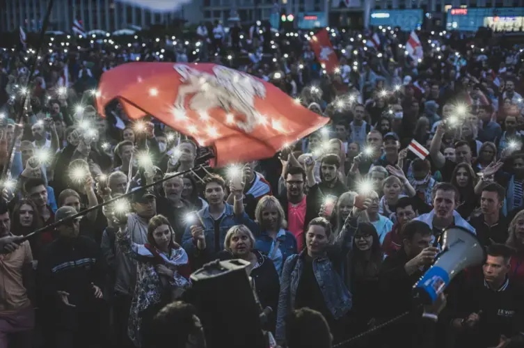 Opposition supporters wave an old Belarusian national flag outside government offices in Minsk. Image by Evgeniy Maloletka. Belarus, 2020.