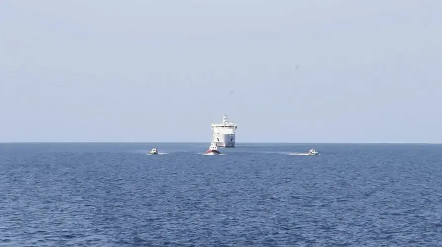 In this April 17, 2020 photo provided by Sea Eye, the Alan Kurdi rescue ship carrying migrants saved from sinking in the Mediterranean approaches a ferry, background center, for a 14-day quarantine. (Sea Eye via AP)