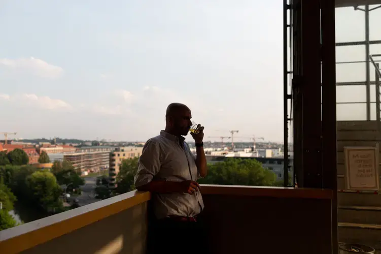 Hamoudi sips a glass of whiskey on the terrace of his office. Image by Bradley Secker. Germany, 2020.