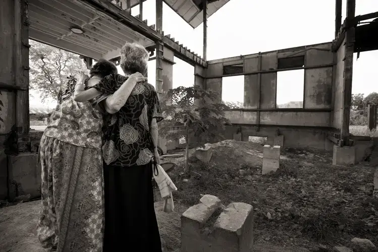 Pilar Quilantang Galang (left) and Belen Alarcon Culala support each other during a visit to the 'Red House,' where the women were repeatedly raped as children by Japanese soldiers during World War II. 'We had a deeply painful experience in this house,' says Galang. 'No amount of money can erase the memories. Because money fades, but awful memories do not. They last forever.' Image by Cheryl Diaz Meyer. Philippines, 2019.