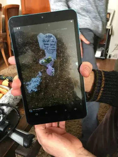 Mahmoud al-Hayek shows a photo of his daughter Rand's gravestone in Greece. Rand, 6, was killed by a train after the family crossed from Turkey into Greece as refugees. Image by Jeanne Carstensen. France.